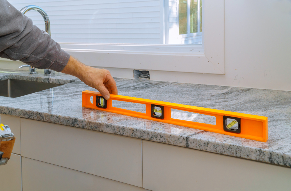 A man inspects a countertop's alignment with a level, demonstrating attention to detail in his home improvement project.